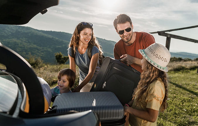 Happy parents and their kids talking while loading their luggage before a trip by car.