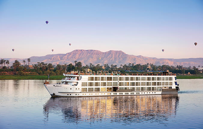 A Uniworld river cruise ship with mountains in background and hot air balloons