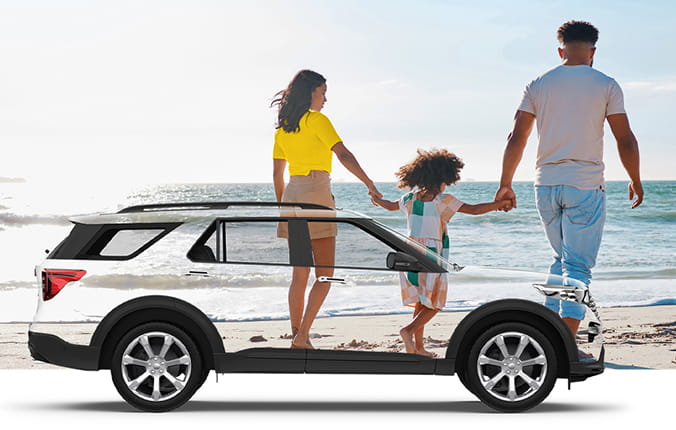 Family of three walks on a beach with the ocean and mountains in background. Transparent SUV in foreground.