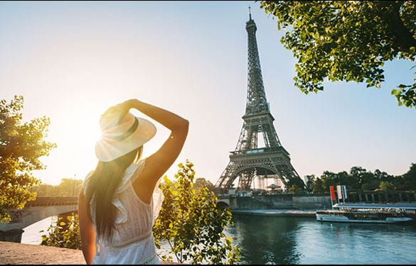 Woman holds her hand to her hat in amazement and gazes at the Eiffel Tower at sunset
