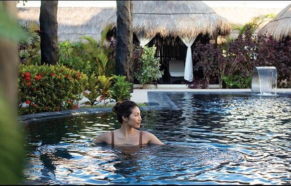 A woman in a pool at a luxury resort with cabanas in background